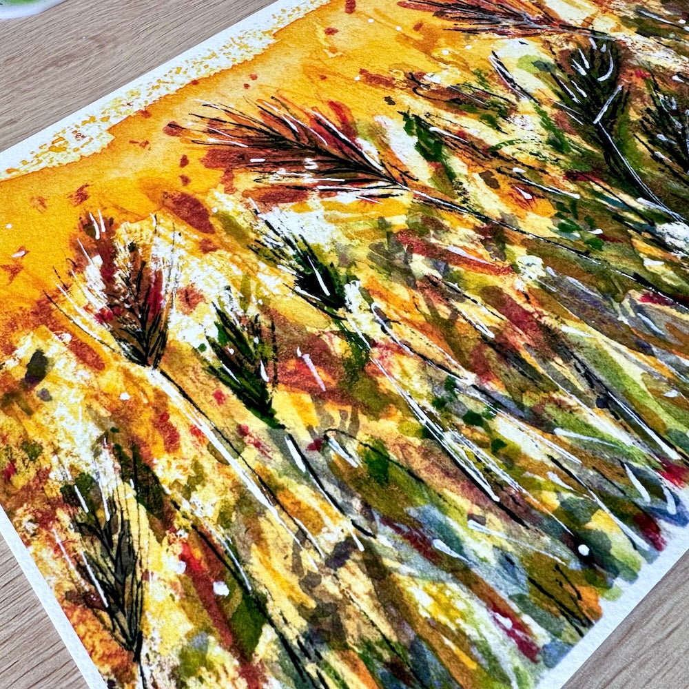 Gros plan d’une illustration aquarelle représentant un champ de blé aux tons chauds et dorés. Les épis sont peints avec des touches dynamiques de jaune, ocre, brun et vert, mettant en valeur la texture du papier et le mouvement naturel de la scène. Appartient à Boutique de Moments.