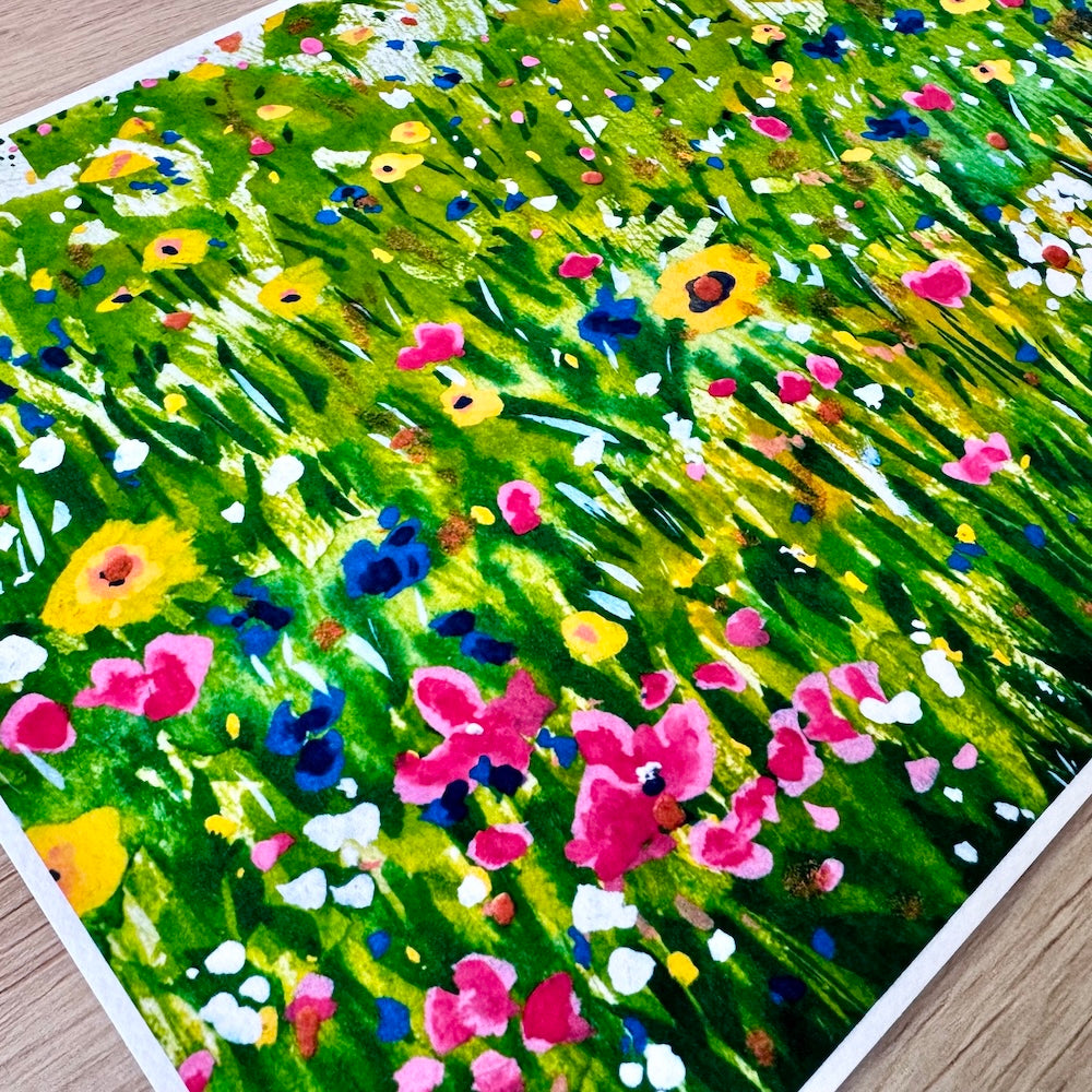 Gros plan d’une illustration aquarelle représentant un champ de fleurs sauvages aux couleurs vives. On y voit des fleurs rouges, jaunes, blanches et bleues se détachant sur un fond vert intense, avec une texture de papier visible qui accentue le rendu artistique et naturel. Appartient à Boutique de Moments.