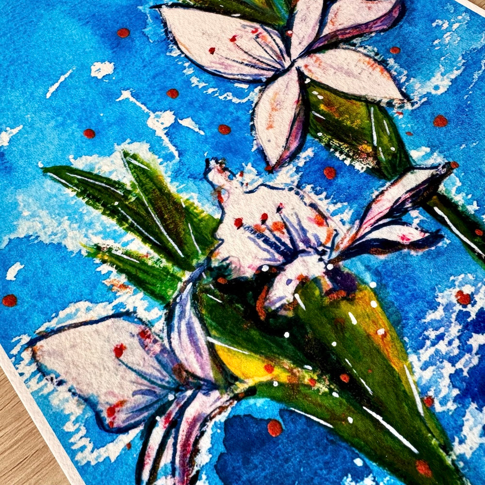 Gros plan d’une illustration aquarelle représentant des glaïeuls blancs avec des touches de rose et d’orange, sur un fond bleu vif texturé. Les feuilles vertes contrastent avec les pétales délicats, et la texture du papier met en valeur les détails et les nuances de la peinture. Appartient à Boutique de Moments.