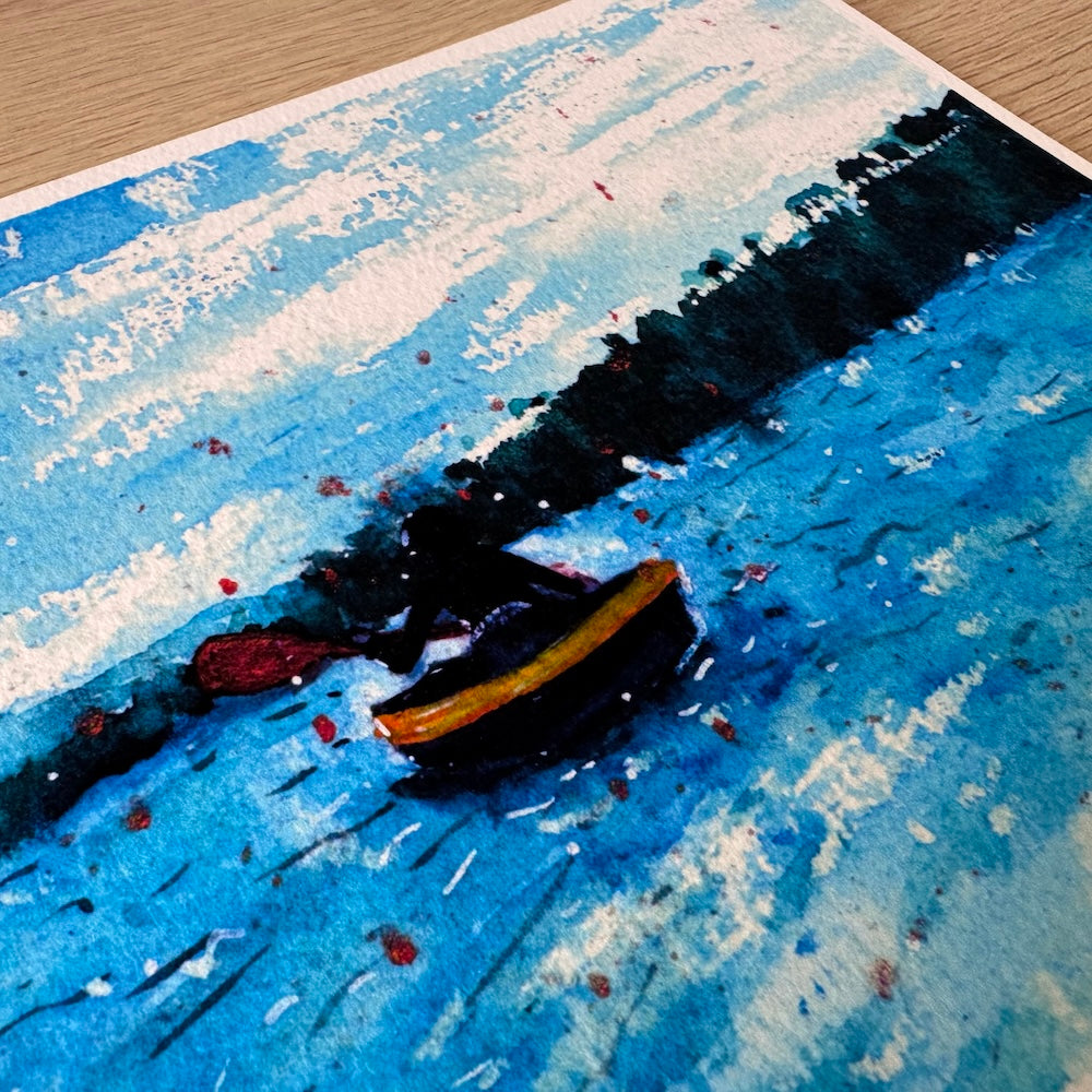 Gros plan d’une illustration aquarelle montrant une personne en kayak jaune pagayant sur un lac aux teintes bleues intenses. La texture du papier met en valeur les reflets de l’eau et la silhouette sombre se détache sur un fond de forêt lointaine et de ciel légèrement nuageux. Appartient à Boutique de Moments.