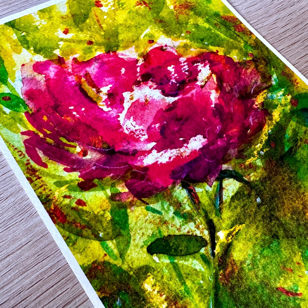 Gros plan d’une illustration aquarelle montrant une fleur rouge aux pétales délicats, entourée de feuillage vert lumineux. Les textures et nuances intenses soulignent la richesse des couleurs et la finesse de la composition florale. Appartient à Boutique de Moments.