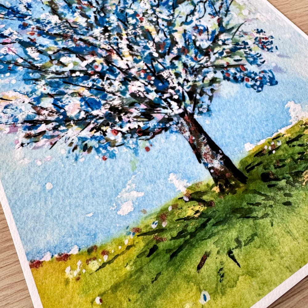Gros plan d’une illustration aquarelle représentant un pommier en fleurs. On distingue les détails de la texture du papier et les touches de couleur vives, évoquant la fraîcheur du printemps sous un ciel bleu lumineux.